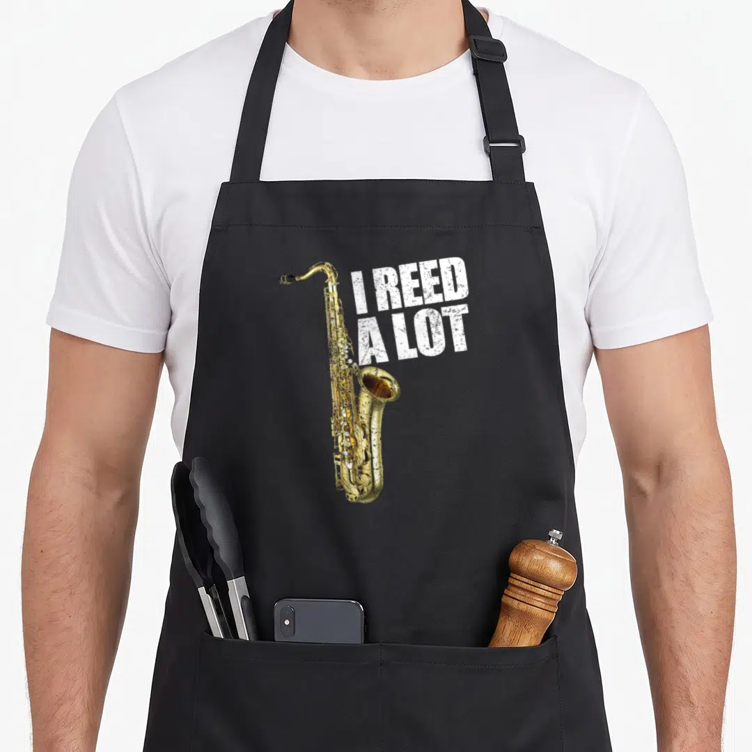 Reed lot of aprons - Gold saxophone next to white distressed text I REED A LOT — shown on a black cotton canvas apron against a white background