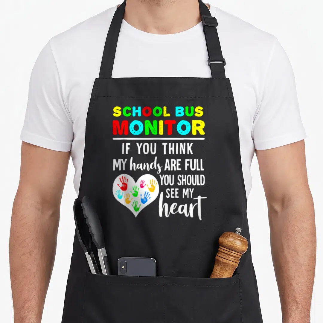 Hand school bus apron - SCHOOL BUS MONITOR text with white heart containing colorful handprints — shown on a black cotton canvas apron against a white background