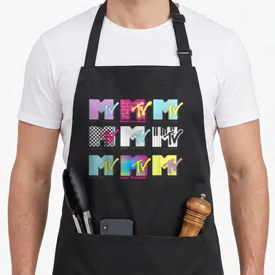 Stack mtv apron - Nine MTV logos in purple, yellow, cyan, pink, black grid with MUSIC TELEVISION text — shown on a black cotton canvas apron against a white background