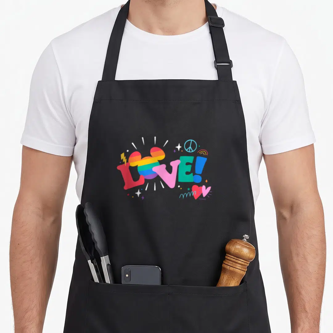 Doodle rainbow apron - LOVE! text with striped mouse head, peace sign, rainbow, stars in red pink blue yellow purple — shown on a black cotton canvas apron against a white background