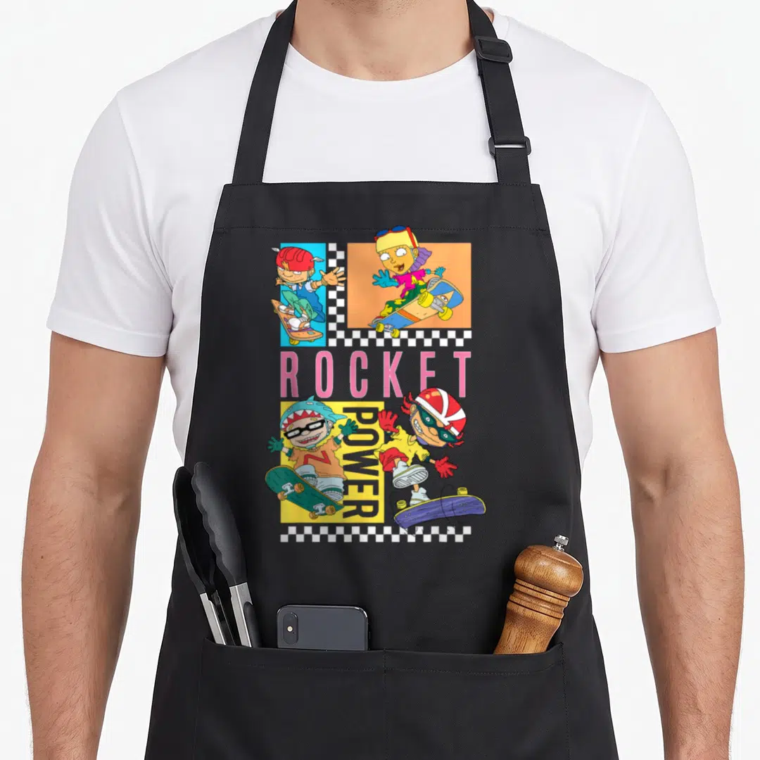 Rocket checkerboard apron - Four cartoon skateboarders in colored boxes surrounding ROCKET POWER text and checkerboard — shown on a black cotton canvas apron against a white background