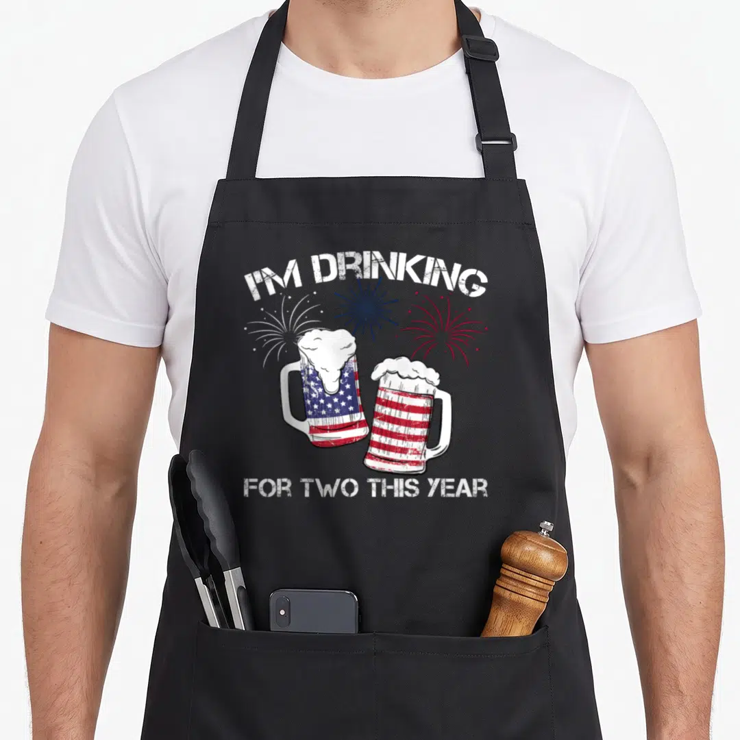 Pregnancy 4th of july apron - Distressed I'm Drinking For Two text with star-spangled beer mugs and fireworks — shown on a black cotton canvas apron against a white background