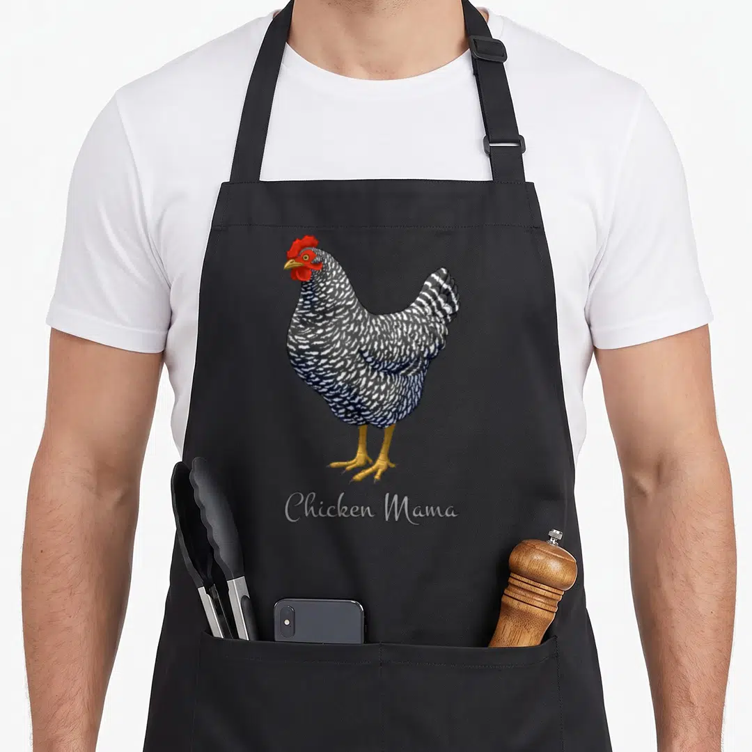 Chicken bird aprons - Cartoon black and white barred hen with red comb above Chicken Mama text — shown on a black cotton canvas apron against a white background