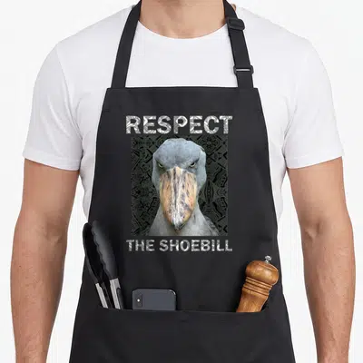 Respect bird apron - Realistic shoebill head with patterned RESPECT THE SHOEBILL text on black background — shown on a black cotton canvas apron against a white background