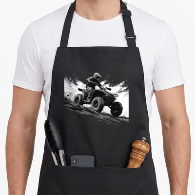 Wheeler racing apron - Black and white illustration of rider on ATV kicking up dirt debris — shown on a black cotton canvas apron against a white background