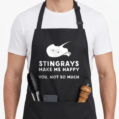 Funny stingray apron - White stingray silhouette above text reading STINGRAYS MAKE ME HAPPY YOU NOT SO MUCH — shown on a black cotton canvas apron against a white background