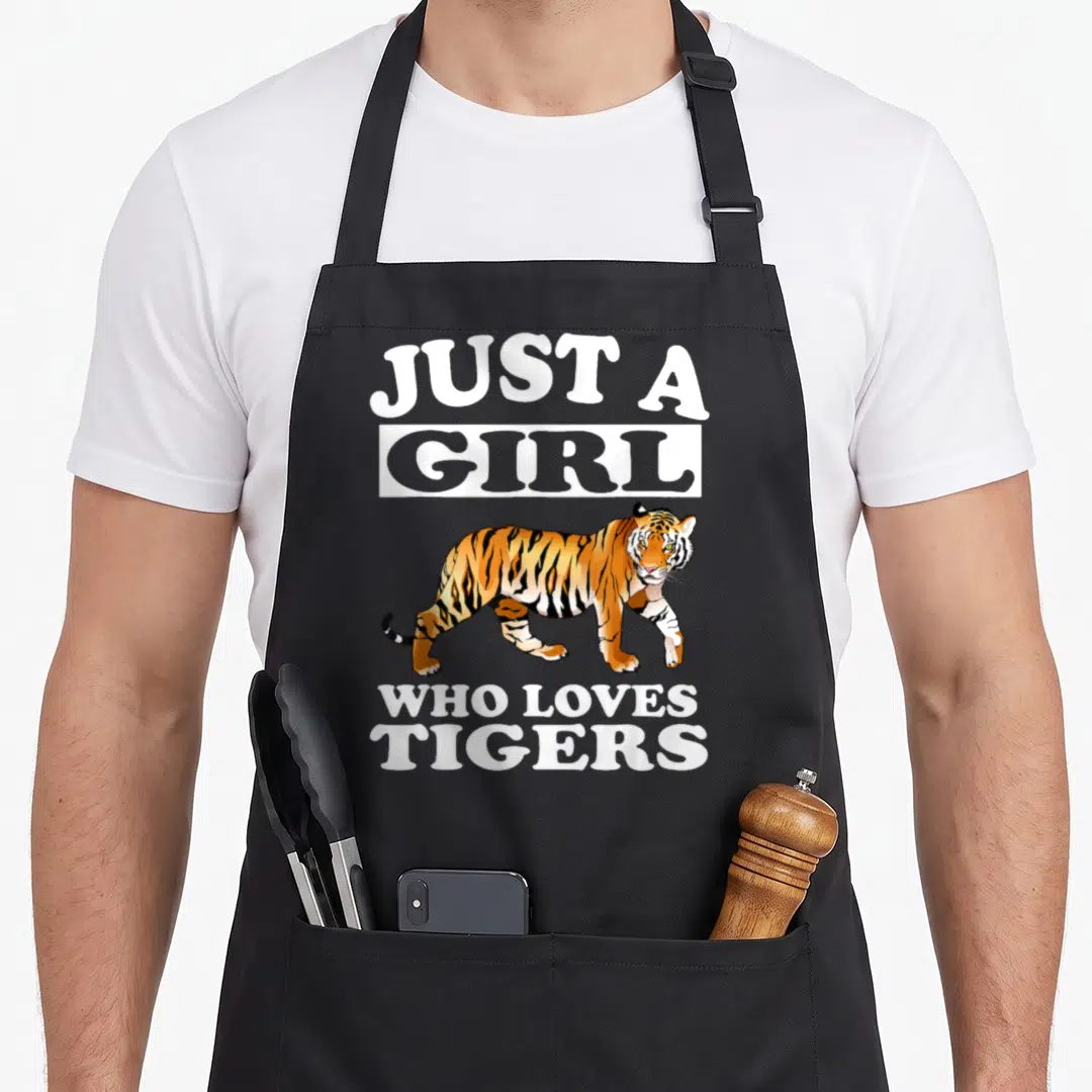 Funny tiger animal apron - Cartoon tiger illustration with Just A Girl Who Loves Tigers text — shown on a black cotton canvas apron against a white background