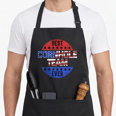 Backyard game aprons - Distressed red white and blue flag text reading Best Cornhole Team Ever with black stars — shown on a black cotton canvas apron against a white background