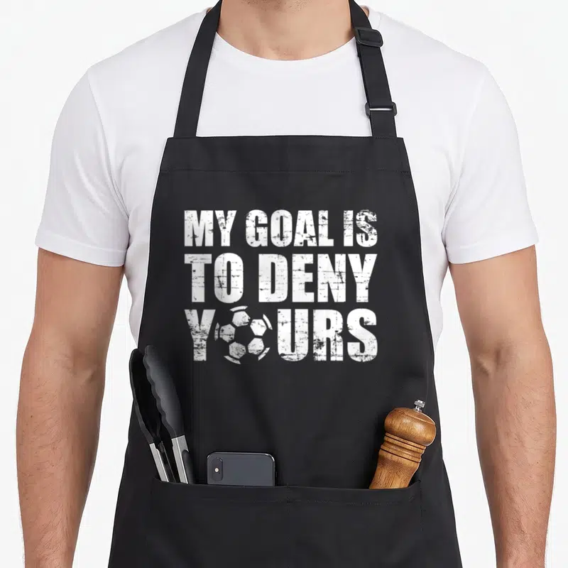 Goal goalkeeper apron - White distressed text reading My Goal Is To Deny Yours with a soccer ball replacing the O — shown on a black cotton canvas apron against a white background