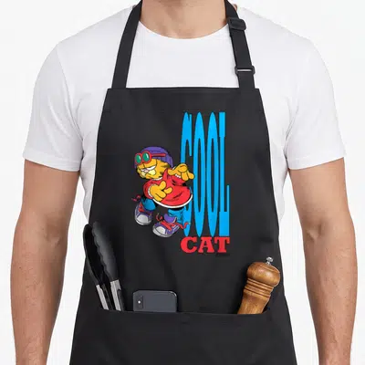 90s cat apron - Cartoon orange cat in purple hat pointing at blue COOL CAT text — shown on a black cotton canvas apron against a white background