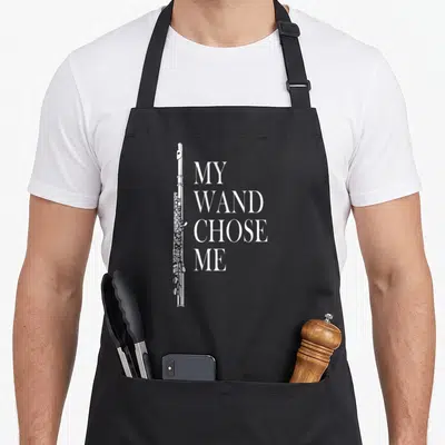 Wand flute apron - Vertical white flute beside stacked text reading My Wand Chose Me in serif font — shown on a black cotton canvas apron against a white background