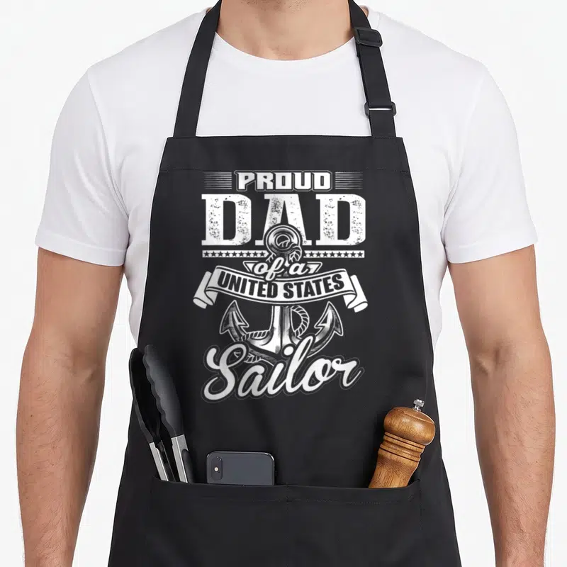 Proud sailor apron - White PROUD DAD of a UNITED STATES Sailor text around an anchor — shown on a black cotton canvas apron against a white background