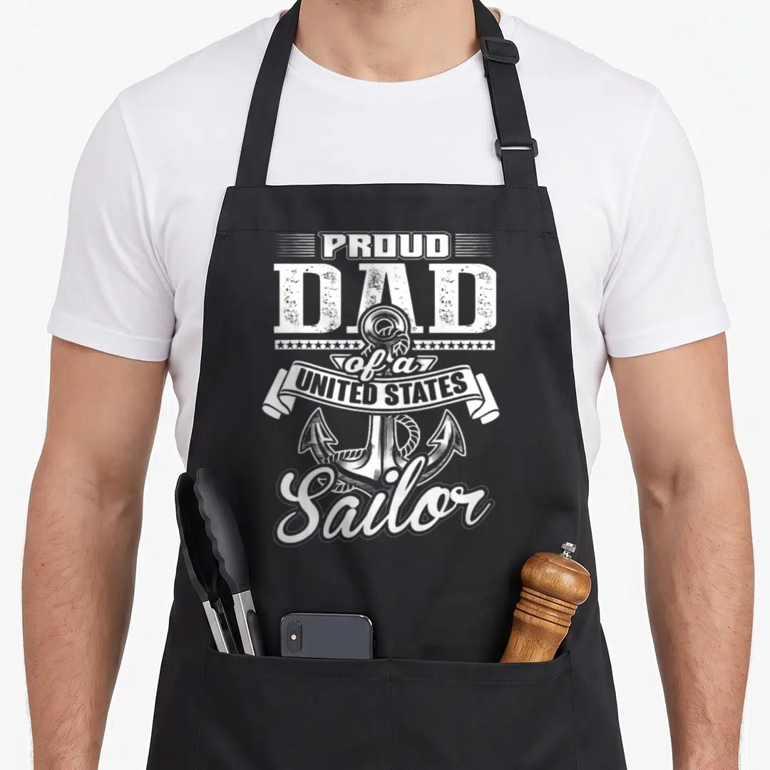 Proud sailor apron - White PROUD DAD of a UNITED STATES Sailor text around an anchor — shown on a black cotton canvas apron against a white background