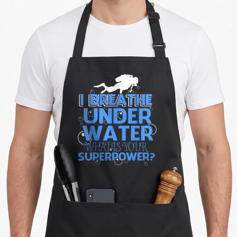 Breathe jellyfish apron - White scuba diver above blue stacked text reading I BREATHE UNDER WATER WHAT IS YOUR — shown on a black cotton canvas apron against a white background