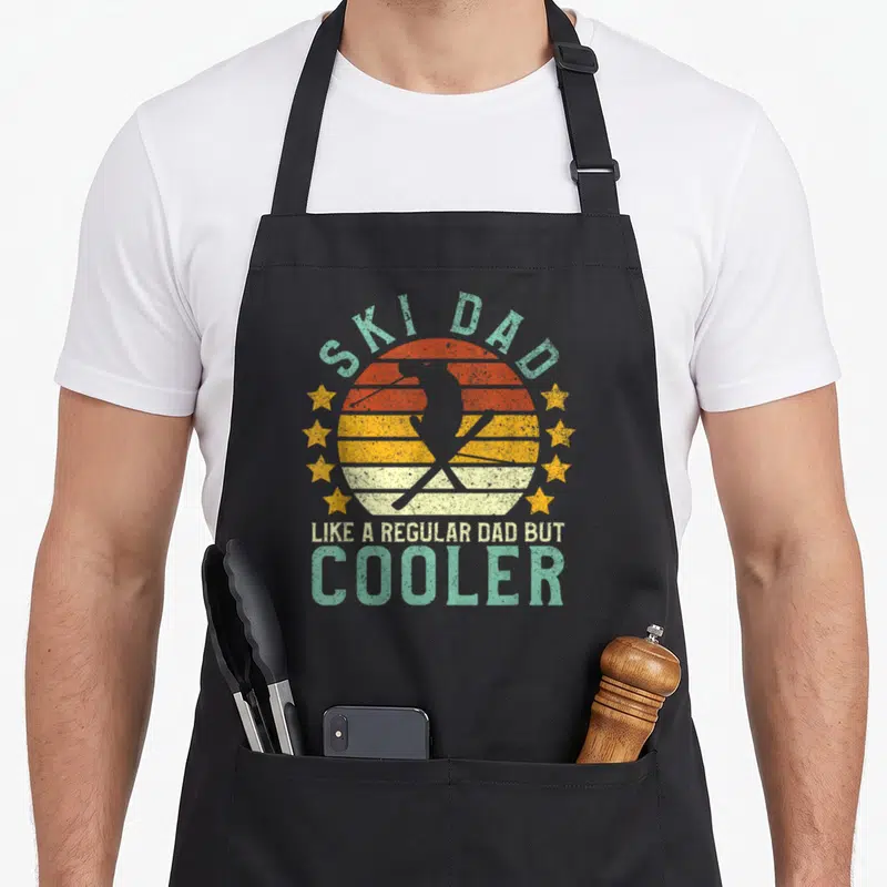 Ski father day apron - Retro striped sun with skier silhouette and text like a regular dad but cooler — shown on a black cotton canvas apron against a white background