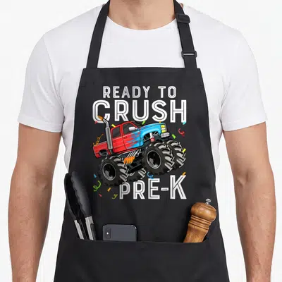 Preschool ready truck apron - Red and blue monster truck with confetti and READY TO CRUSH PRE-K text — shown on a black cotton canvas apron against a white background