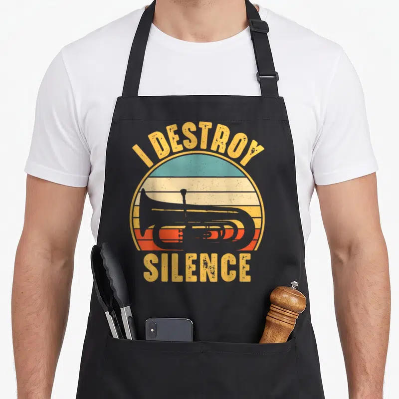 Destroy tuba apron - Grey tuba silhouette inside retro striped sun with text I DESTROY SILENCE — shown on a black cotton canvas apron against a white background