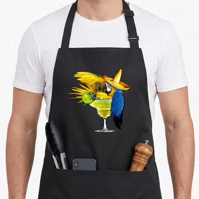 Parrot holiday apron - Cartoon macaw in sombrero perched on margarita glass holding lime slice — shown on a black cotton canvas apron against a white background