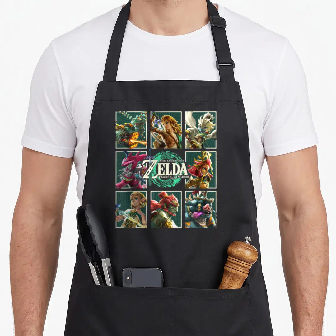 Kingdom character aprons - Zelda Tears of Kingdom 3x3 grid character portraits with sword logo in green and gold — shown on a black cotton canvas apron against a white background