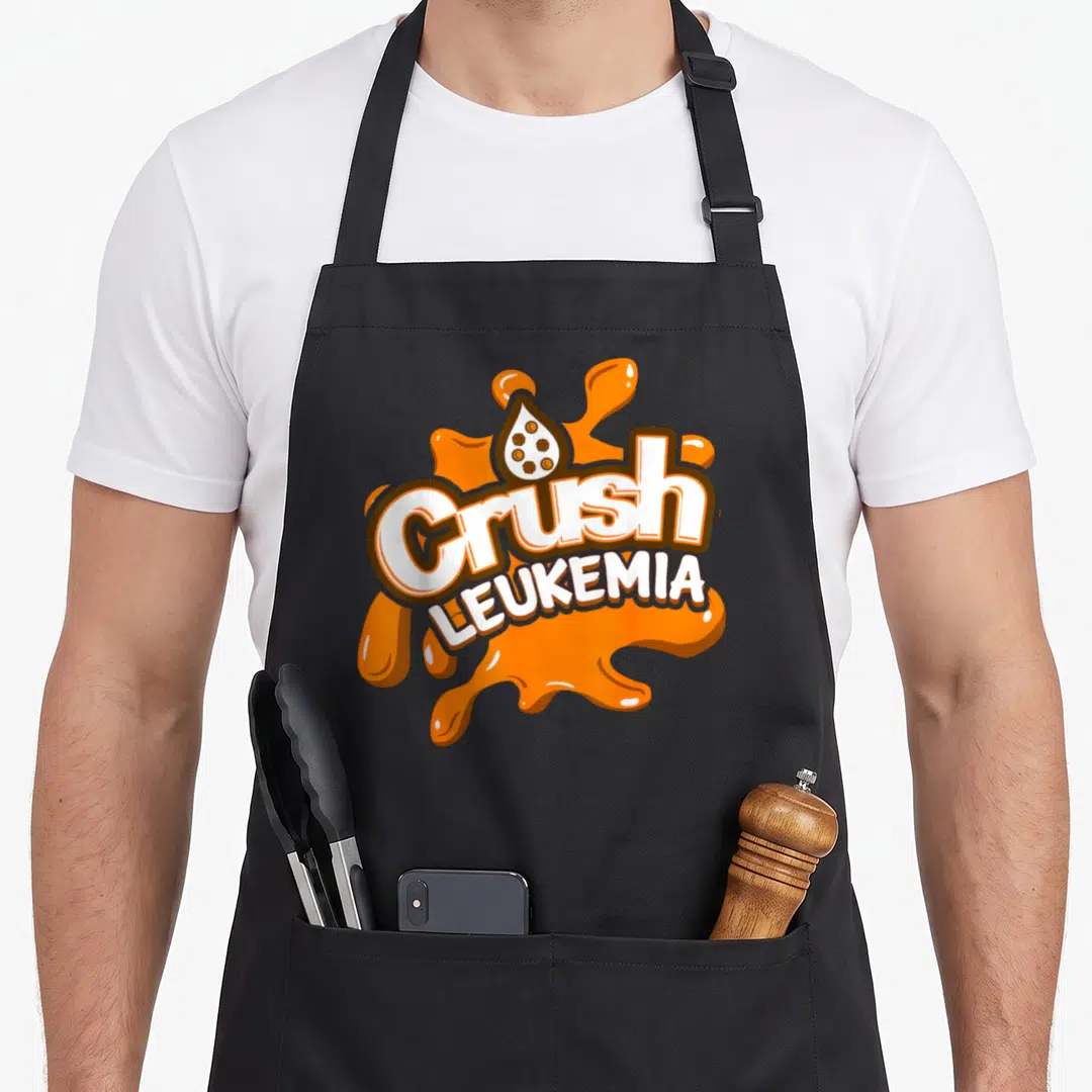 Crush blood apron - Orange splash graphic with white text reading Crush Leukemia and a droplet containing brown shapes — shown on a black cotton canvas apron against a white background