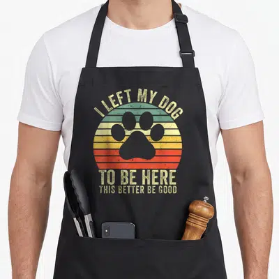 Funny left dog apron - Retro striped circle with paw print and text I LEFT MY DOG TO BE HERE THIS BETTER BE GOOD — shown on a black cotton canvas apron against a white background