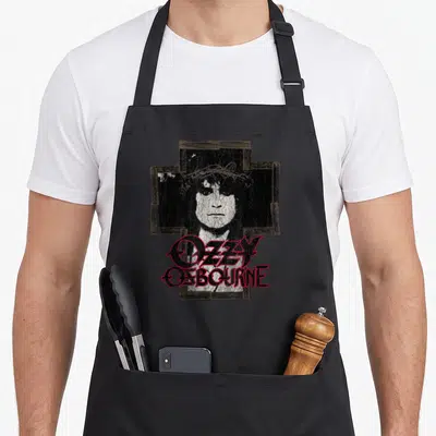 Ozzy cross apron - Distressed cross with man's face and red OZZY OSBOURNE lettering — shown on a black cotton canvas apron against a white background