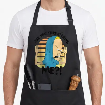 Beavis judge apron - Cartoon man with raised hands and Are You Threatening Me text over striped sun — shown on a black cotton canvas apron against a white background