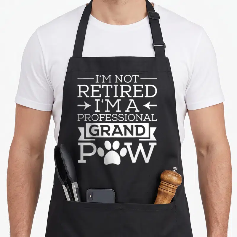 Grand paw dog apron - White text I'm not retired professional grand pow with paw print replacing O on black apron — shown on a black cotton canvas apron against a white background