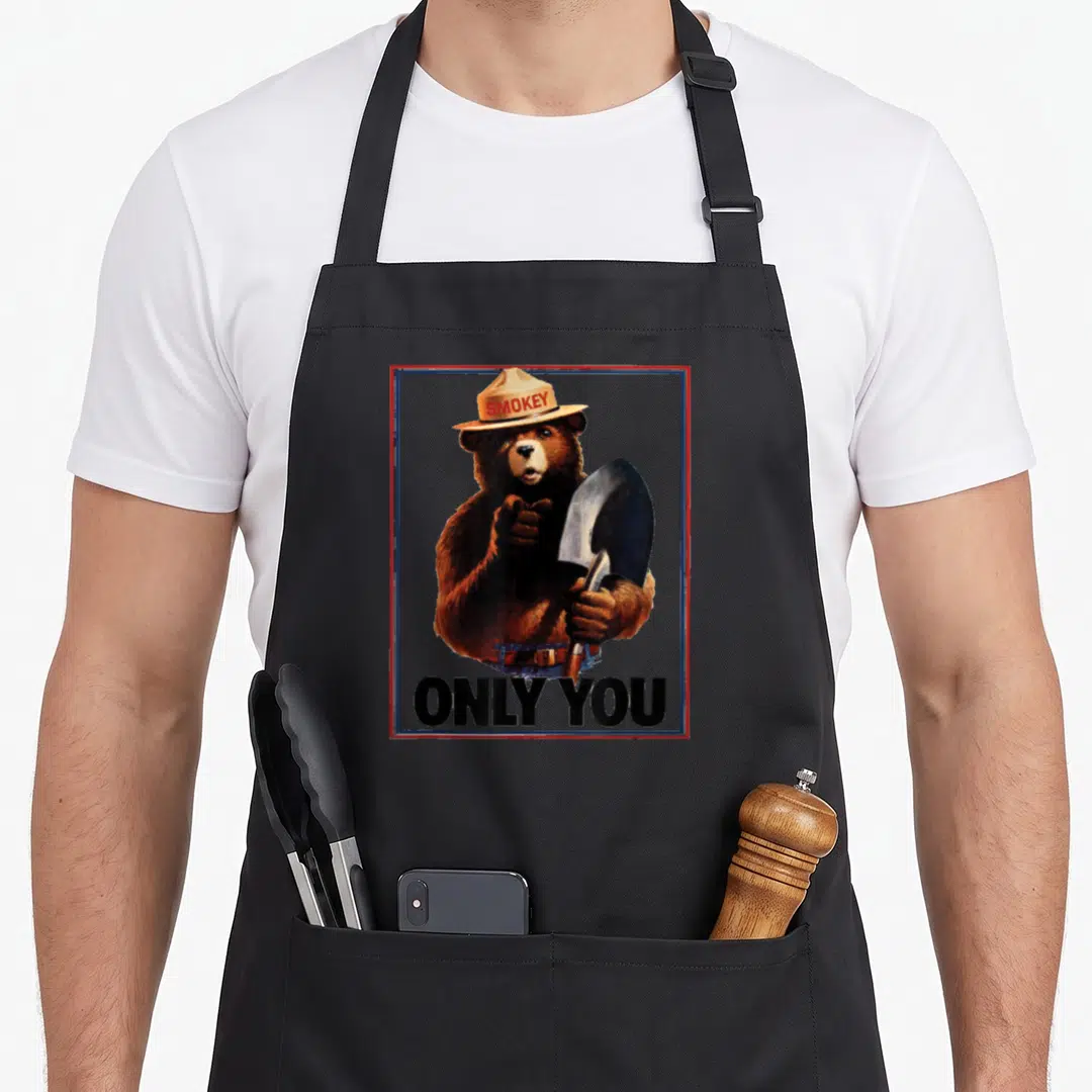 Patriotic bear apron - Realistic brown bear with shovel and SMOKEY hat inside red blue border — shown on a black cotton canvas apron against a white background