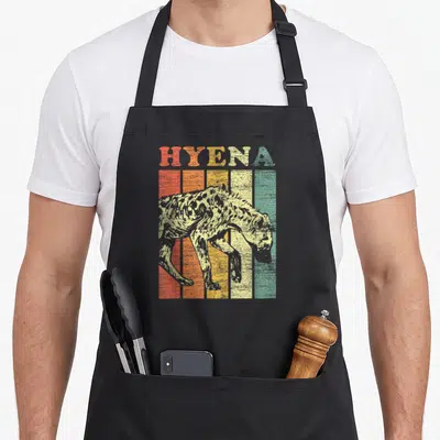 Hyena animal retro apron - HYENA text over five colored vertical stripes with walking hyena silhouette in retro style — shown on a black cotton canvas apron against a white background
