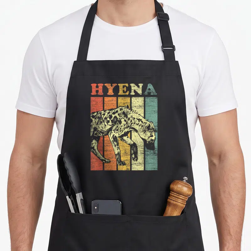 Hyena animal retro apron - HYENA text over five colored vertical stripes with walking hyena silhouette in retro style — shown on a black cotton canvas apron against a white background