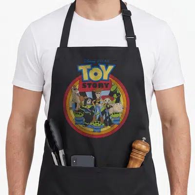 Circle dog breed aprons - Vintage Toy Story logo with Woody Buzz and aliens in red yellow circle — shown on a black cotton canvas apron against a white background
