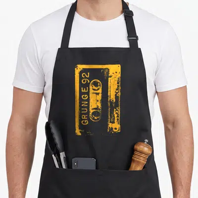 Grunge 90s apron - Distressed orange cassette tape with vertical GRUNGE 92 text — shown on a black cotton canvas apron against a white background