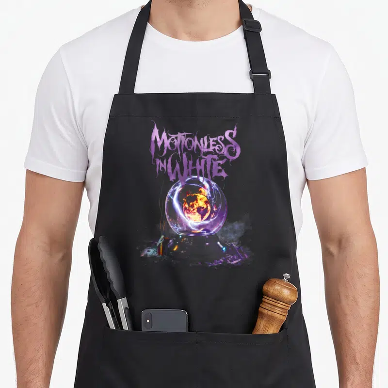 Motionless big band apron - Stylized purple text above crystal ball with fiery earth and lightning — shown on a black cotton canvas apron against a white background