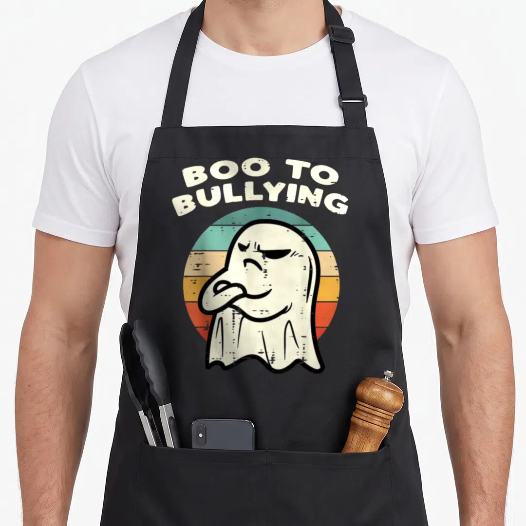 Bullying halloween apron - Cartoon ghost with crossed arms in front of teal yellow orange red stripes under arched text — shown on a black cotton canvas apron against a white background