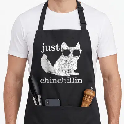 Chinchillin pet apron - White distressed chinchilla wearing glasses with just chinchillin text — shown on a black cotton canvas apron against a white background