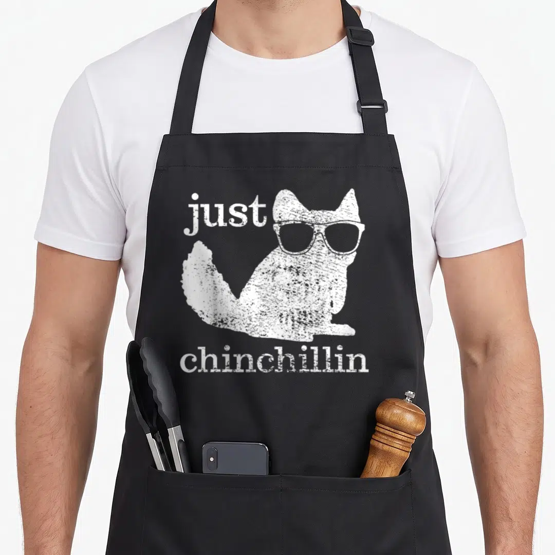 Chinchillin pet apron - White distressed chinchilla wearing glasses with just chinchillin text — shown on a black cotton canvas apron against a white background