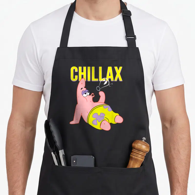 Chillax its birthday apron - Patrick Star reclining and blowing a bubble under yellow CHILLAX text — shown on a black cotton canvas apron against a white background