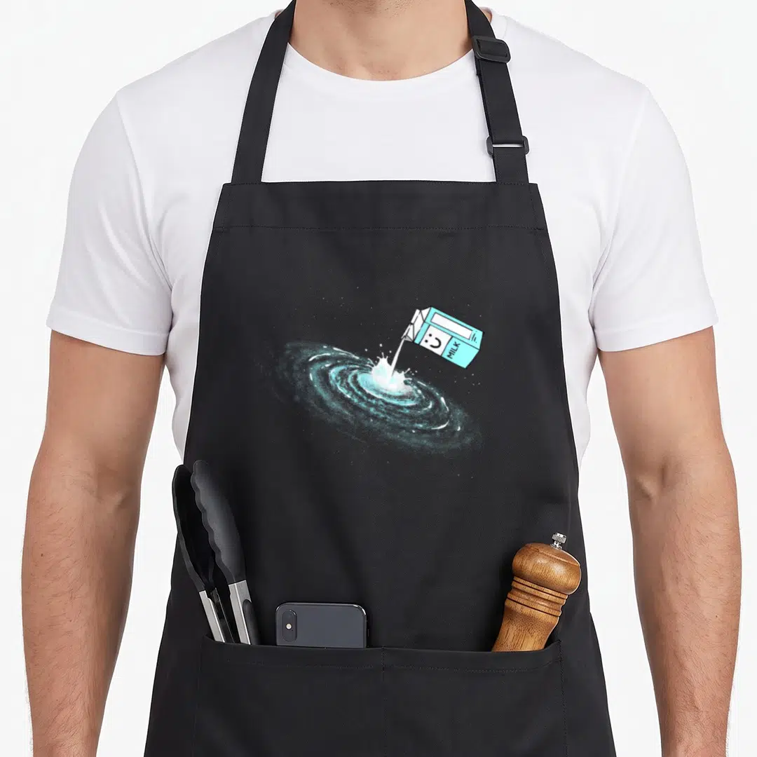 Milky astronomy apron - Tilted blue milk carton pouring white liquid into a swirling blue galaxy spiral — shown on a black cotton canvas apron against a white background