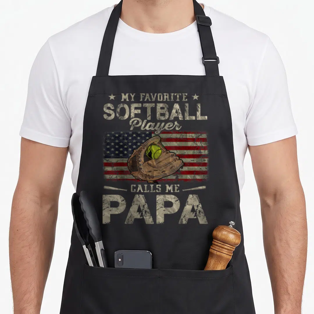 Softball player father day apron - Retro My Favorite Softball Player Calls Me Papa text with glove and distressed flag — shown on a black cotton canvas apron against a white background