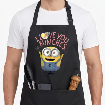 Bunch general apron - Yellow minion with raised arms under pink text reading I Love You Bunches with a heart symbol — shown on a black cotton canvas apron against a white background