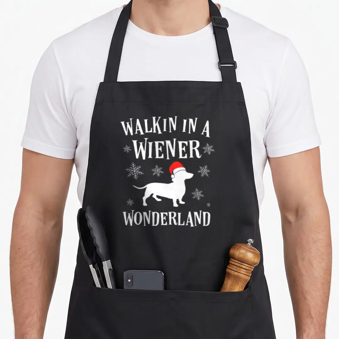 Buncho holiday christmas aprons - Dachshund in red Santa hat with text Walkin in a Wiener Wonderland and snowflakes — shown on a black cotton canvas apron against a white background