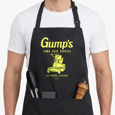 Forrest service apron - Yellow Gump's Lawn Care Service text and push mower graphic with Greenbow Alabama label — shown on a black cotton canvas apron against a white background