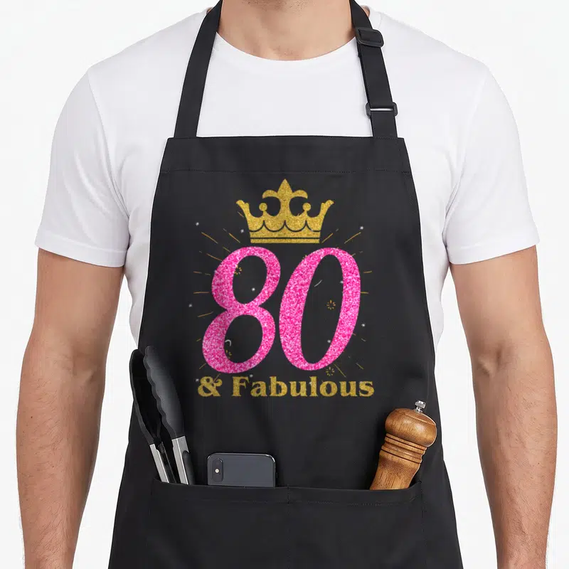 80th fabulous queen apron - Pink glittery number 80 with gold crown and text & Fabulous below — shown on a black cotton canvas apron against a white background