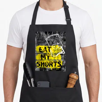 Eat simpson apron - Bart Simpson head outline overlapping stacked Eat My Shorts text on yellow splatter — shown on a black cotton canvas apron against a white background