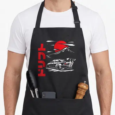 Jdm japan apron - Vertical red Japanese text beside a white drift car and red sun over a mountain — shown on a black cotton canvas apron against a white background