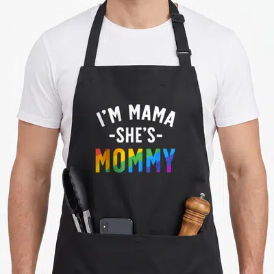 Lesbian mama apron - Stacked text I'M MAMA SHE'S MOMMY with rainbow gradient letters — shown on a black cotton canvas apron against a white background