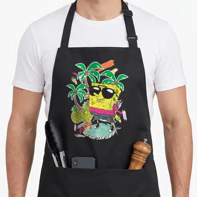 Squarepant tropical print aprons - SpongeBob in sunglasses with palm trees, pineapples, and colorful brushstrokes — shown on a black cotton canvas apron against a white background