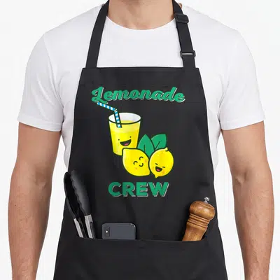 Lemonade lemon apron - Cartoon lemonade glass with straw and two smiling lemons with green text — shown on a black cotton canvas apron against a white background