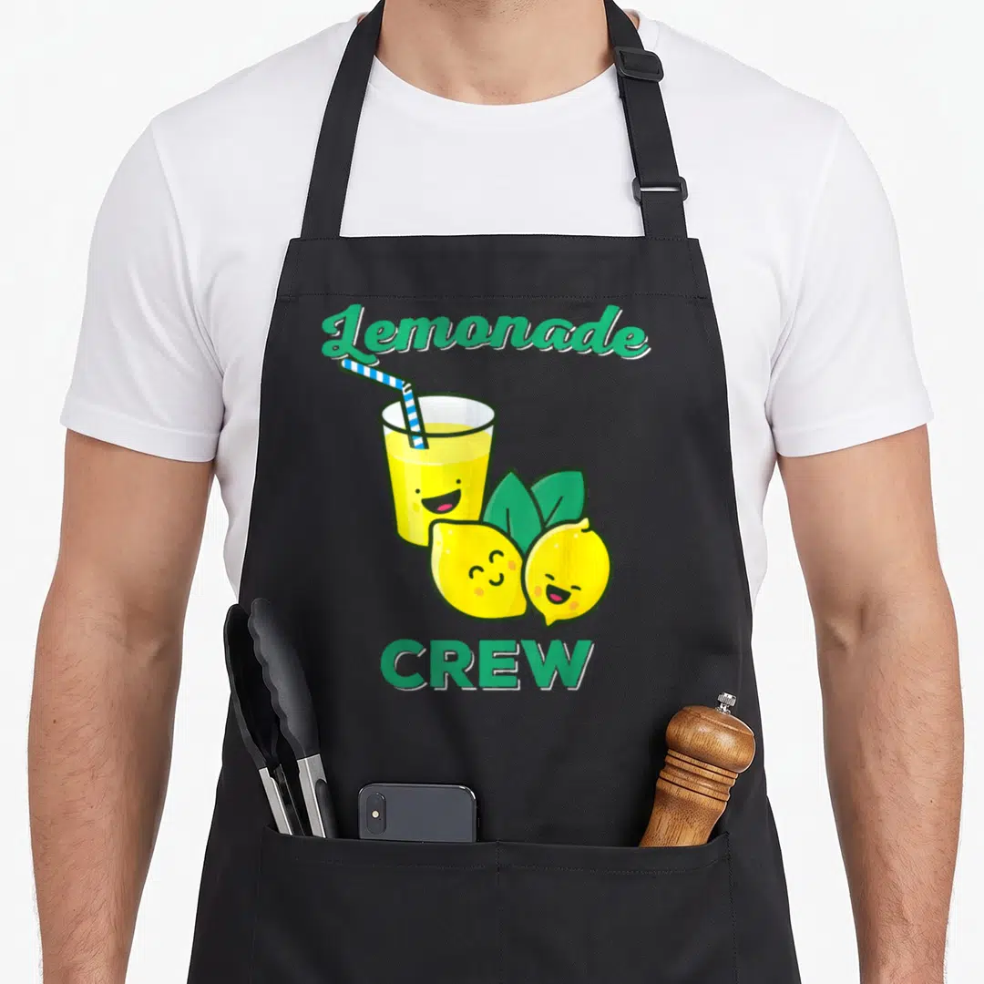 Lemonade lemon apron - Cartoon lemonade glass with straw and two smiling lemons with green text — shown on a black cotton canvas apron against a white background